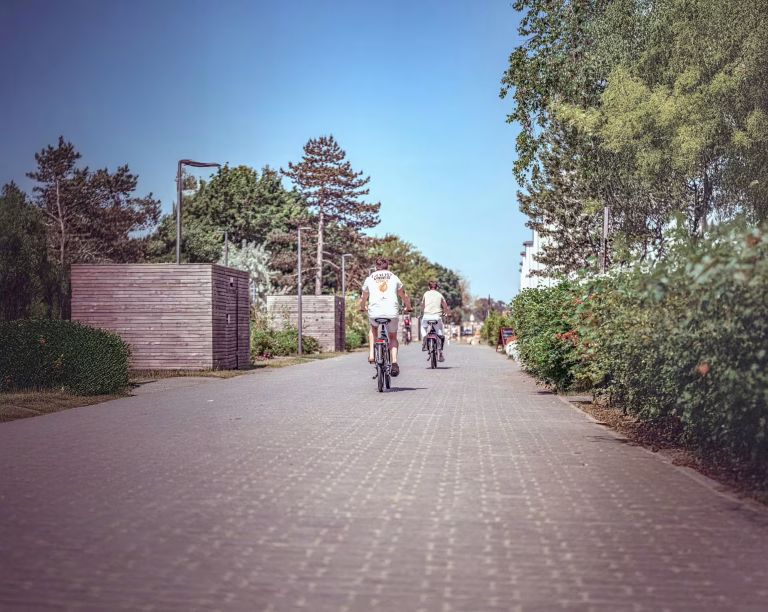 Zwei Personen fahren mit Fahrrädern über einen ruhigen, begrünten Weg nahe der Küste bei Sonnenschein – entspannter Fahrradurlaub und aktive Erholung in maritimer Umgebung